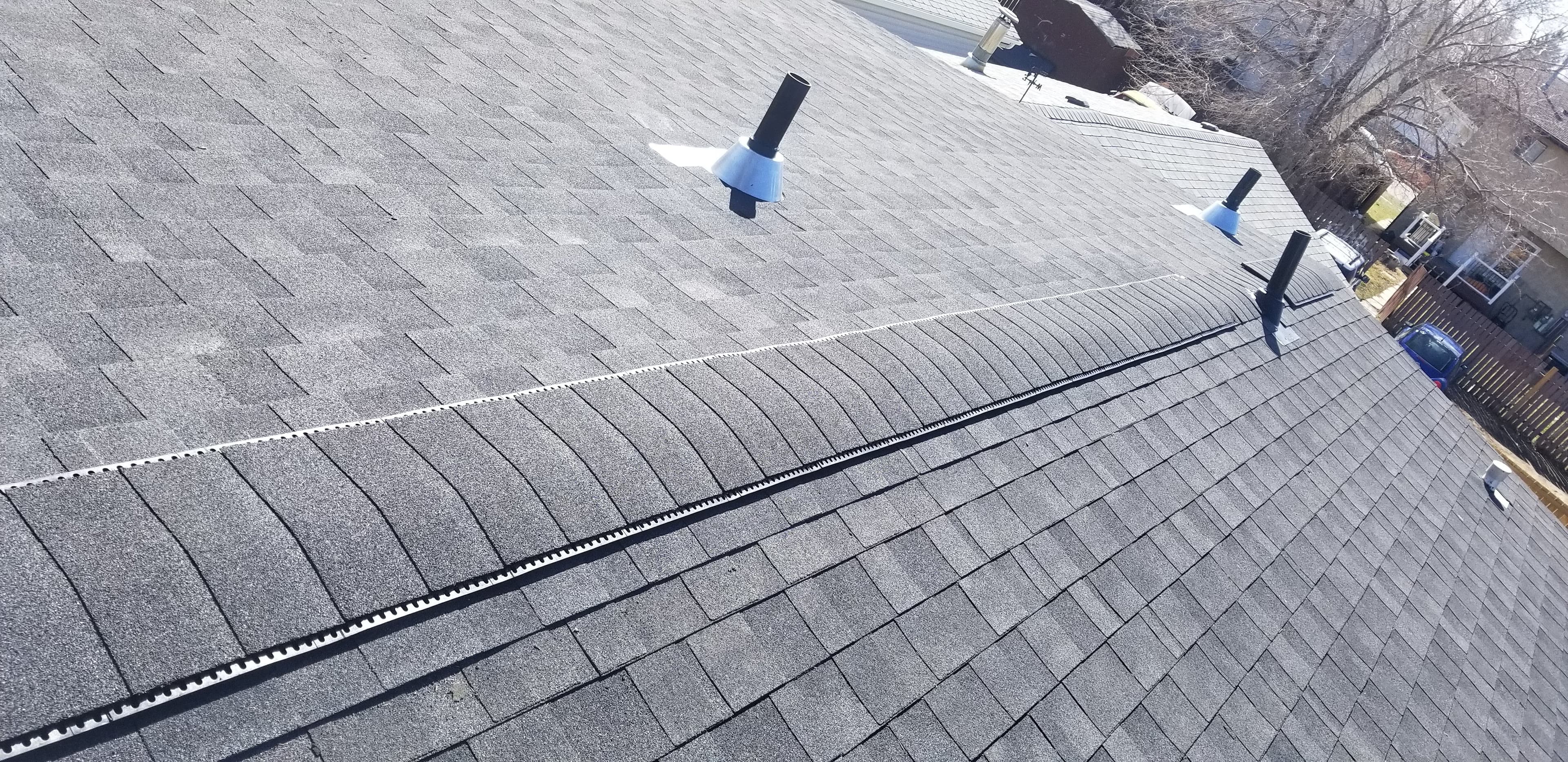 Grey shingled roof with a ridge vent and three black plumbing vent pipes.