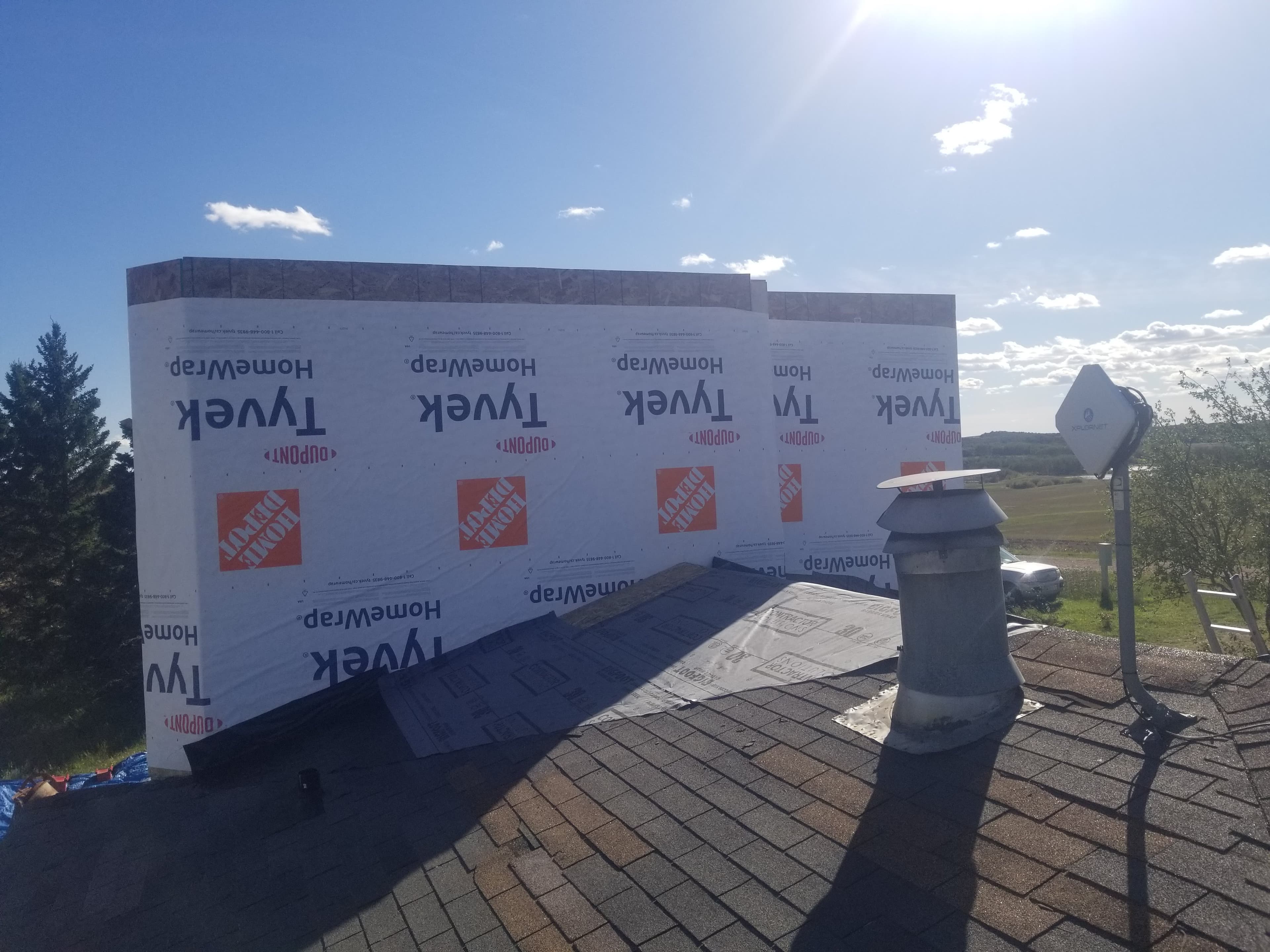 Shingled roof under construction featuring Tyvek HomeWrap, a chimney vent, and a satellite dish.