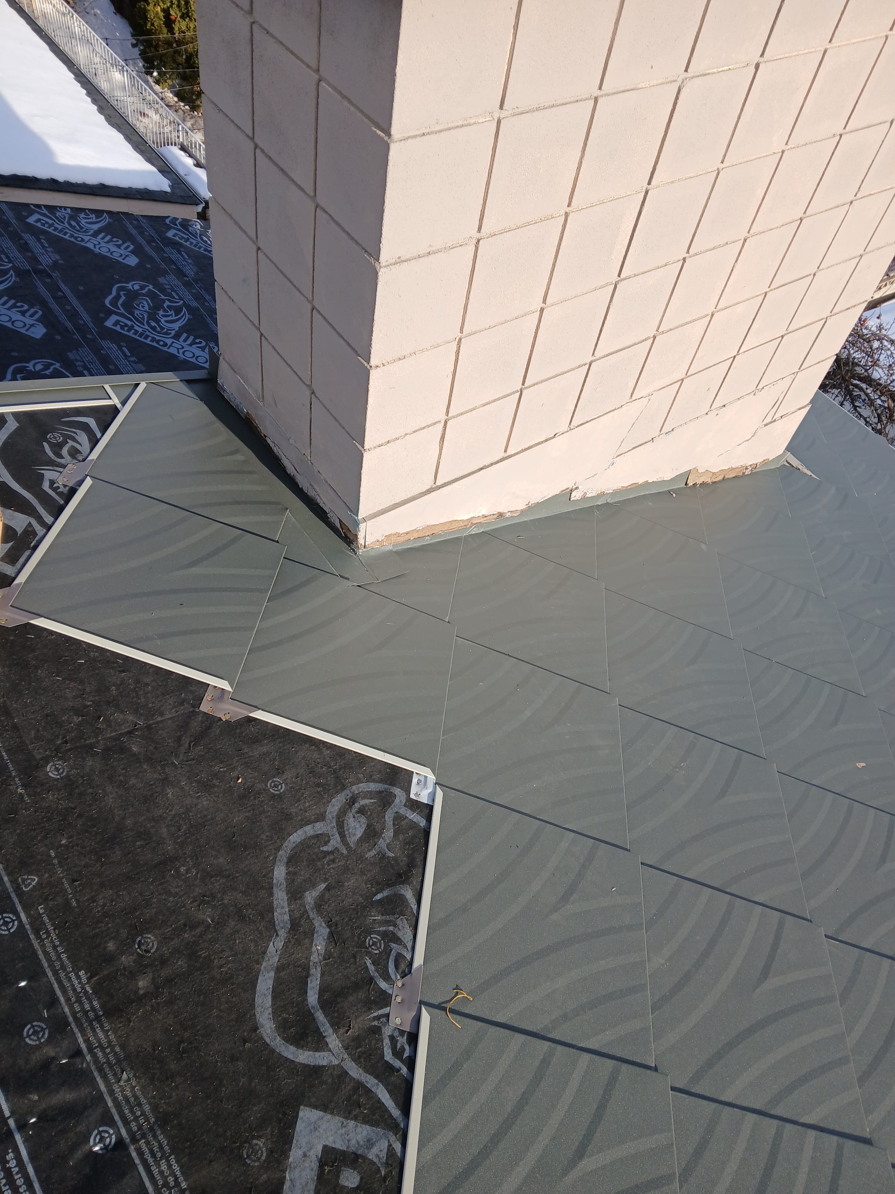 Gray patterned roof tiles installed next to a light-colored tiled chimney over black underlayment.