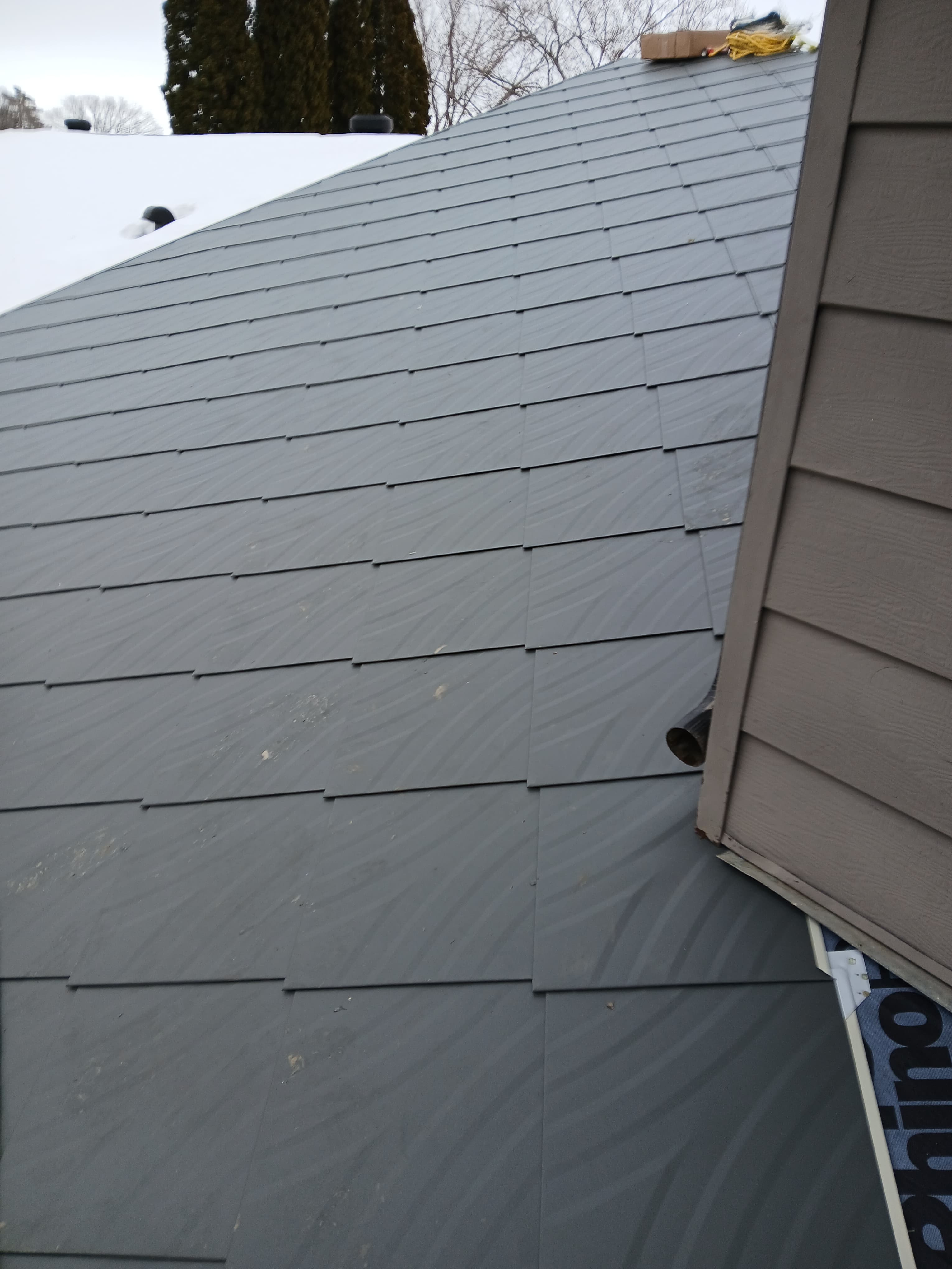 Grey rectangular roof shingles installed in a staggered pattern meeting brown horizontal wall siding.