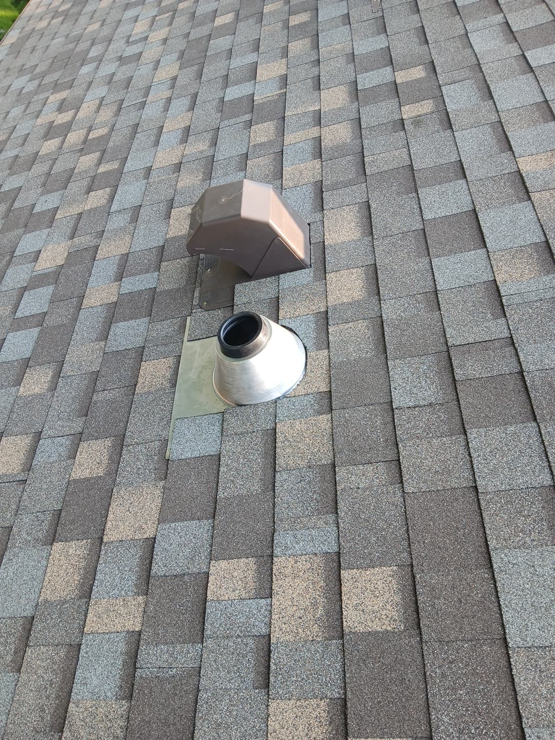 Brown plastic hood vent and silver metal pipe vent on a grey architectural shingle roof.