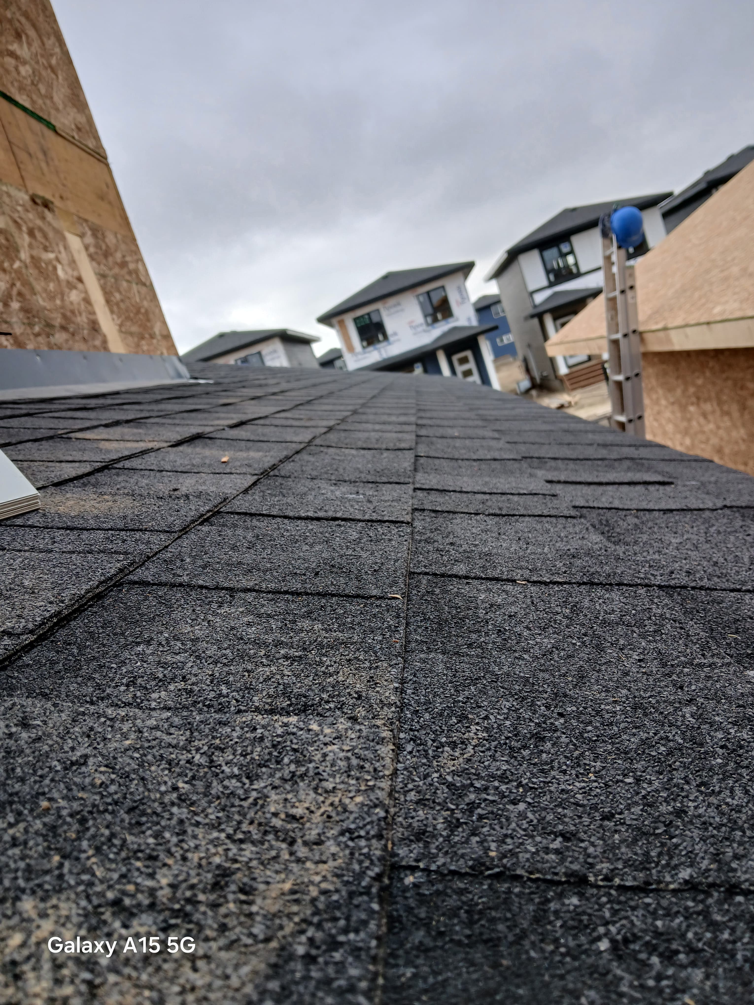 Close-up of dark grey asphalt shingles on a roof overlooking a residential construction site.