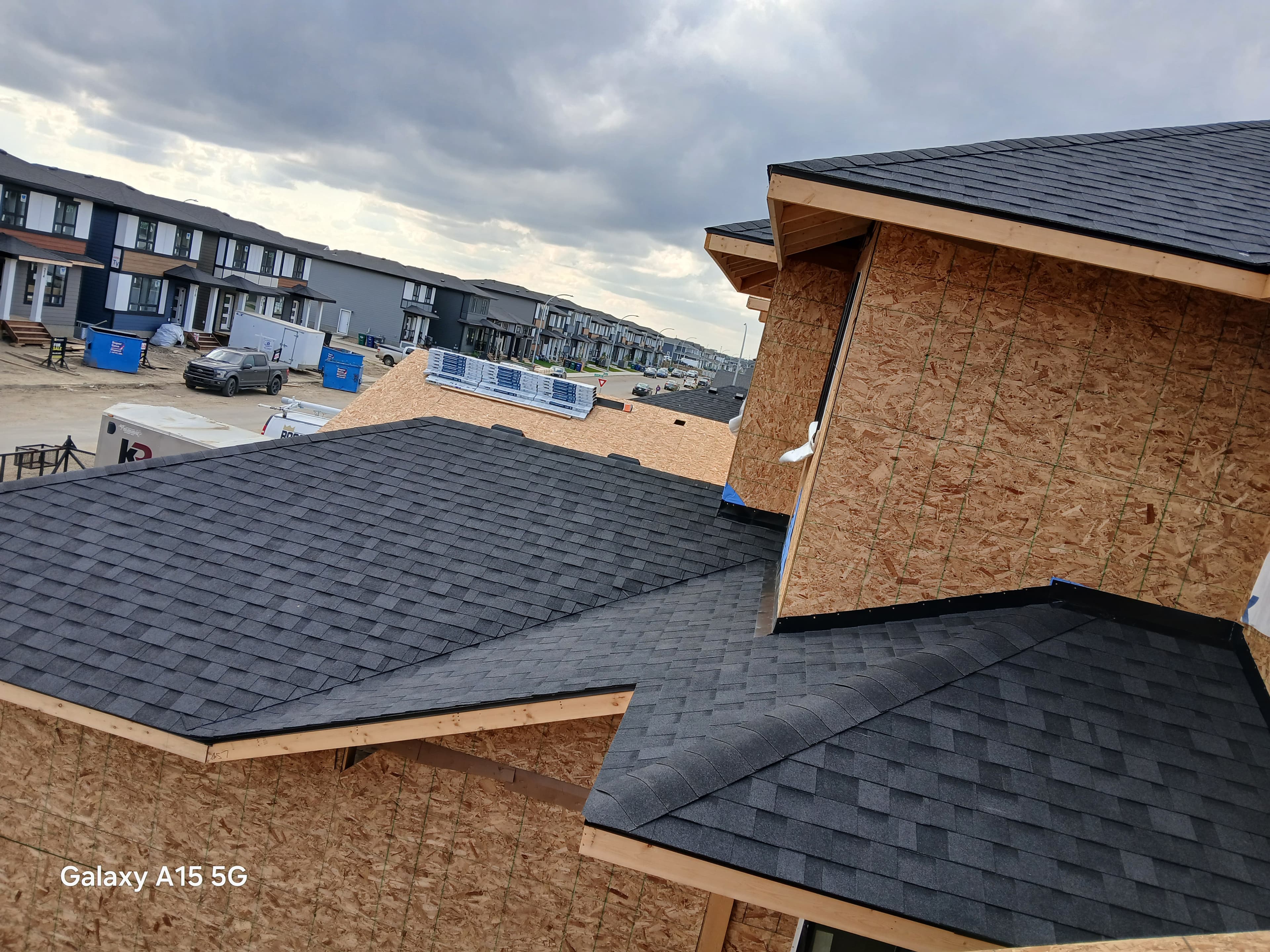 Dark grey asphalt shingles installed on a new plywood roof structure in a suburban neighborhood.
