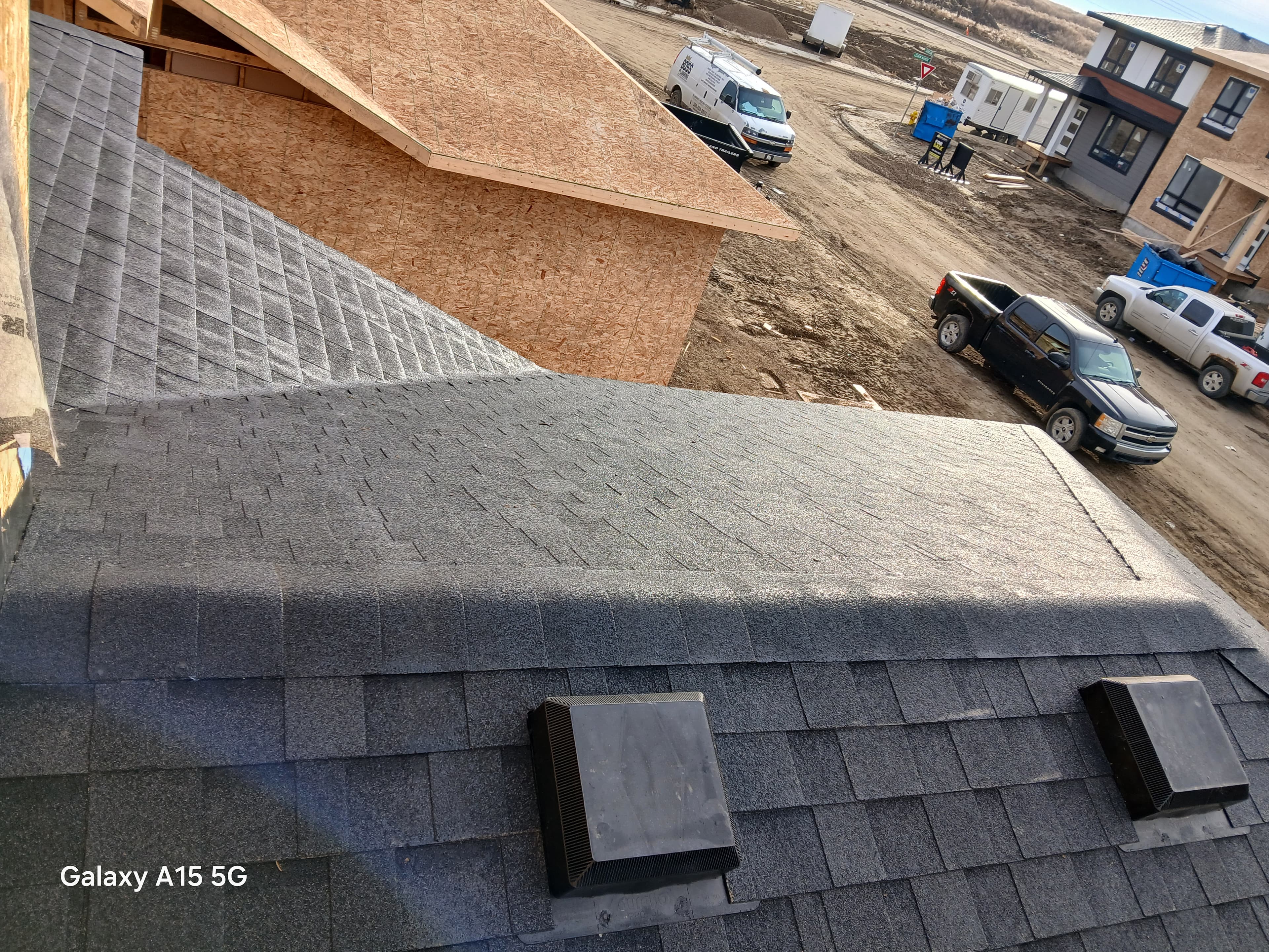 Grey asphalt shingles and vents on a roof under construction overlooking a dirt construction site.