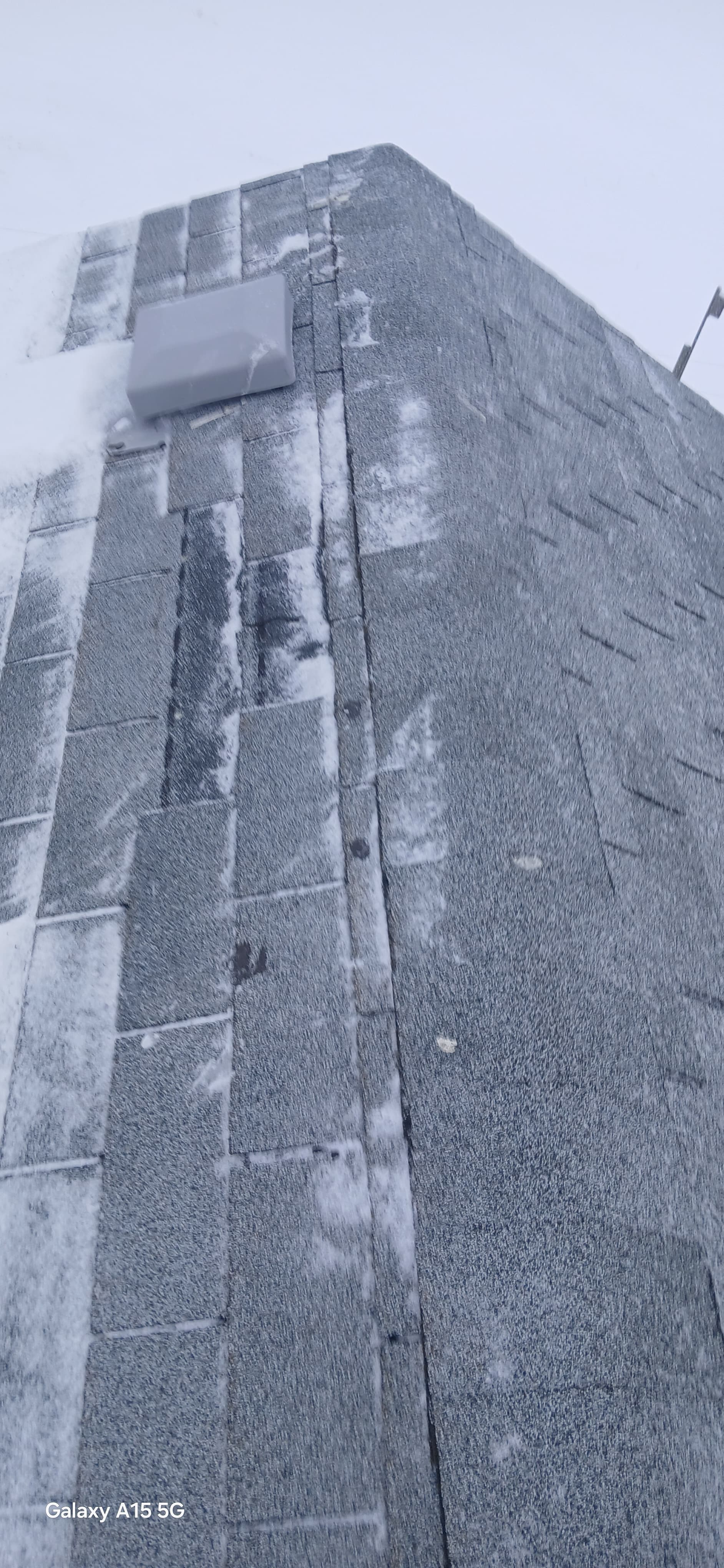 Gray shingled roof and stone wall partially covered in a light dusting of winter snow.