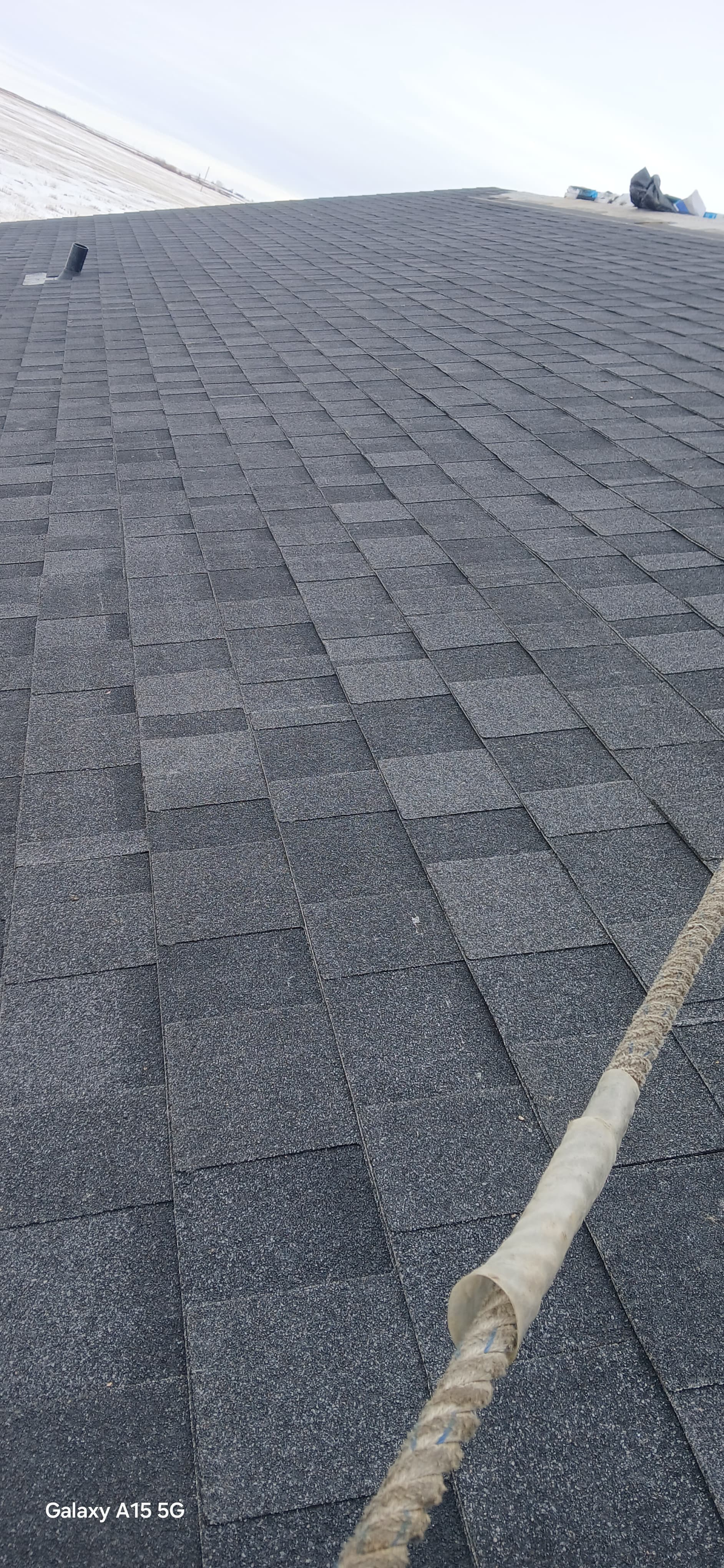 Dark grey asphalt shingles on a roof with a thick rope and white sleeve.